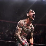 Tattooed male boxer in a ring screams with clenched fists and audience in the background.