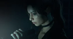 Young woman in a dark room, with blue-tinted light, looking down while holding a glowing handheld device.