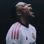 Soccer player in a white Real Madrid jersey screaming with mouth wide open against a dark background.