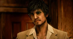 Man wearing a brown blazer and open-collar shirt with a gold chain, sporting sunglasses, in a wood-paneled setting.